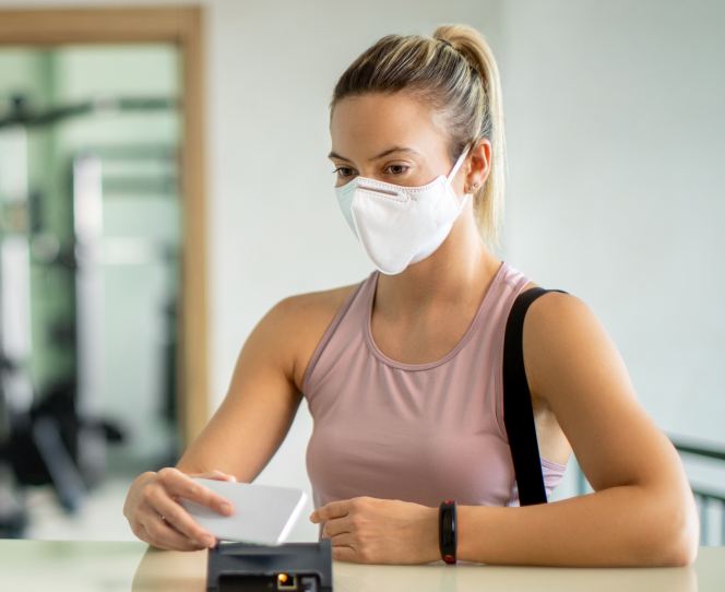 Woman in workout clothes waiting at a customer support desk with a mask on 