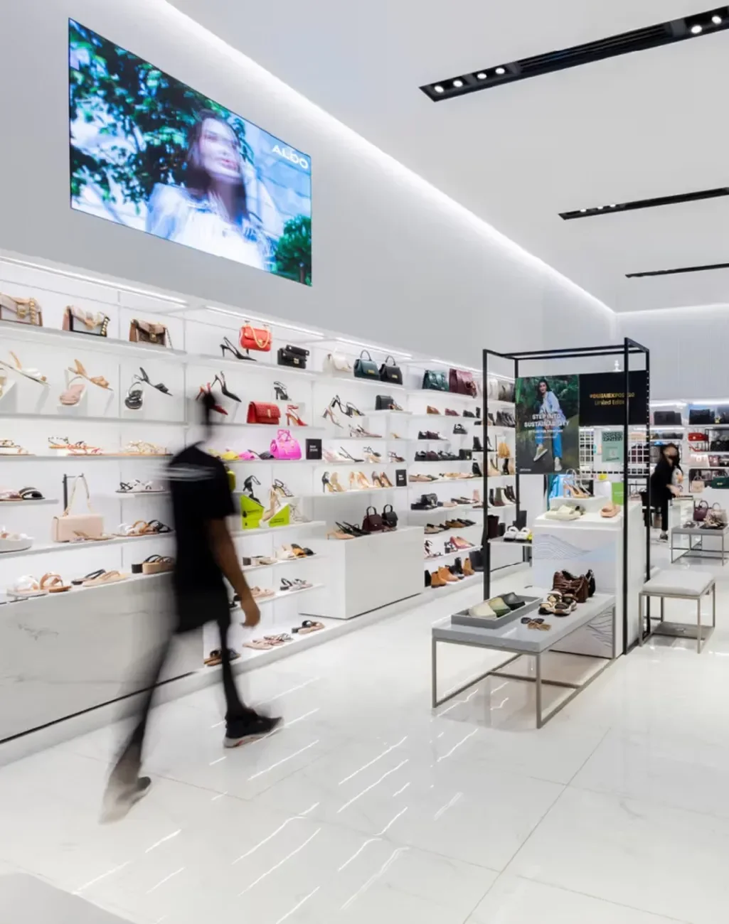 Modern shoe store interior with shoes displayed on white shelves and a person walking by.
