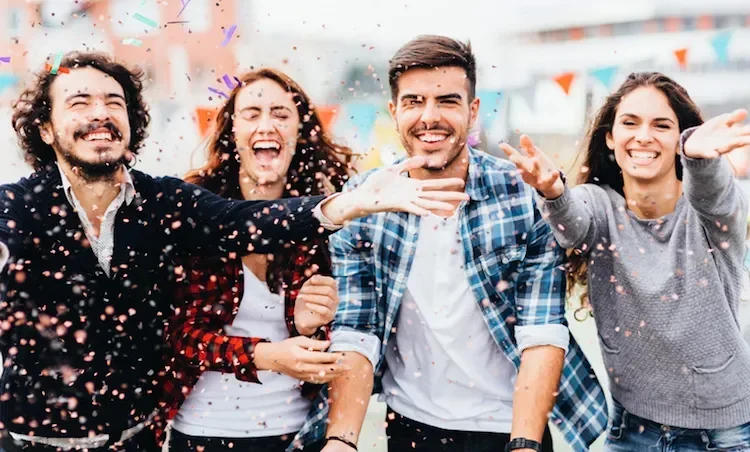 4 happy people throw confetti and laugh at the camera
