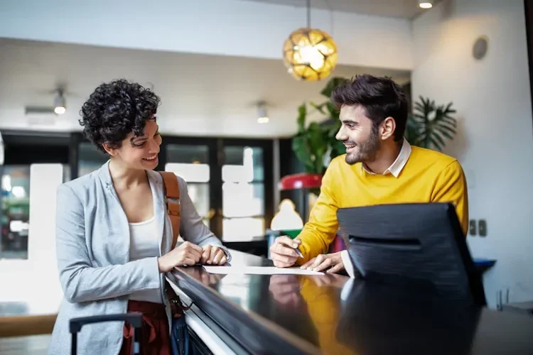 A woman checking in to a hotel A man behind the reception desk smiles at her