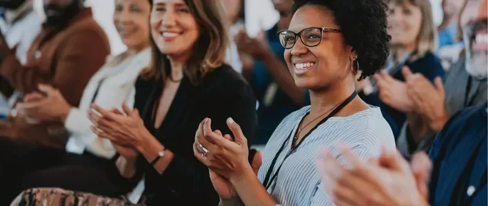 A diverse group of people clapping and smiling at an event.