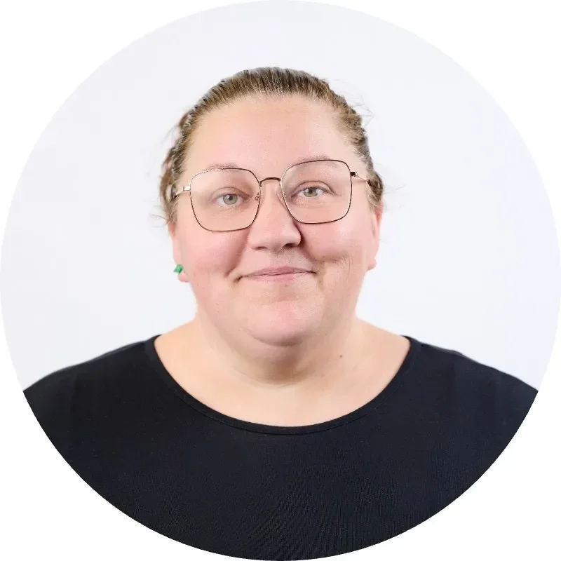Woman with glasses and earrings, smiling against a white background.