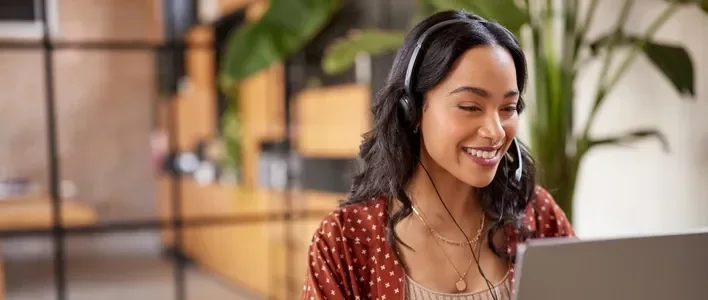 Smiling woman with headphones working on a laptop in a bright, modern office.