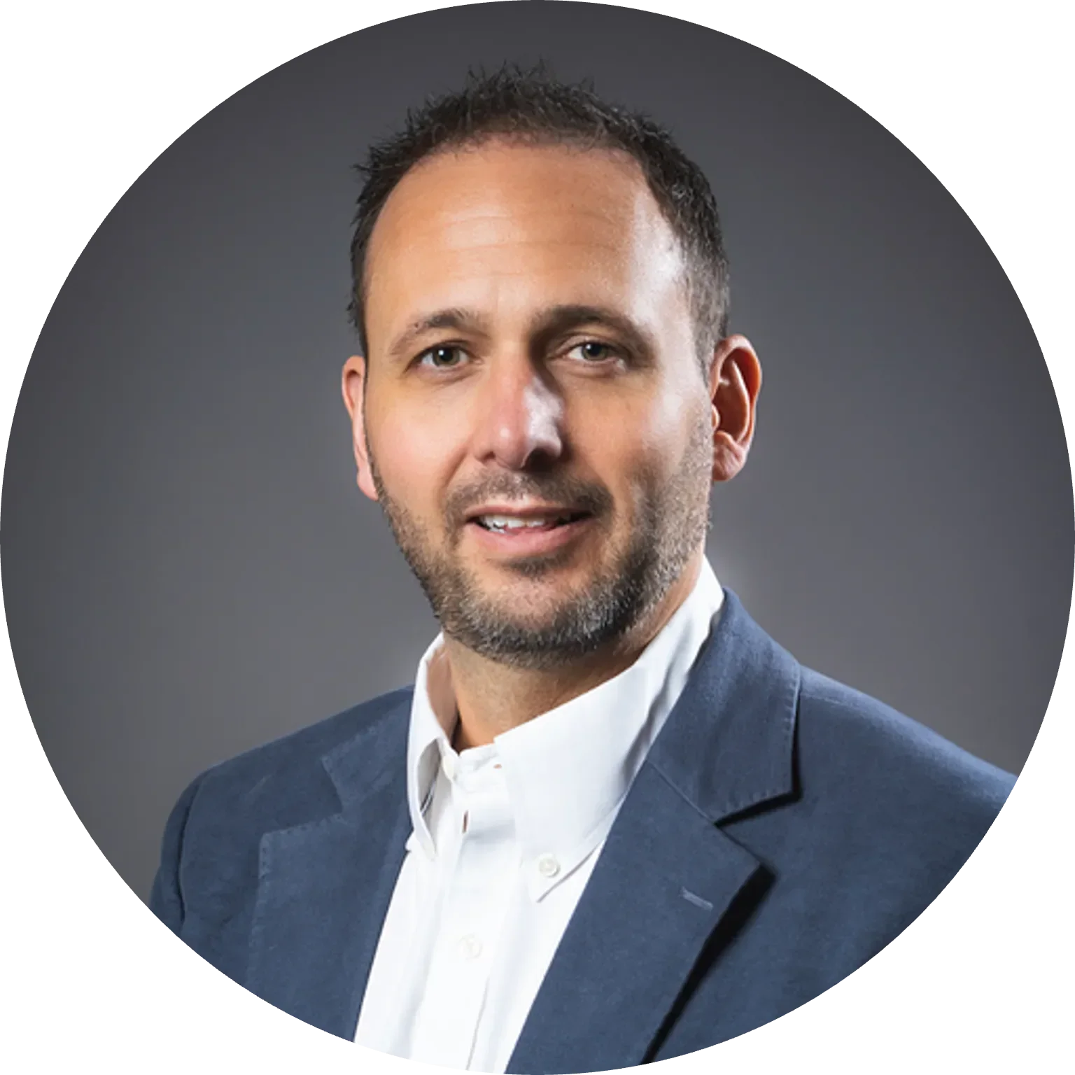 Man with short dark hair, smiling, wearing a blue blazer and white shirt, on a gray background.