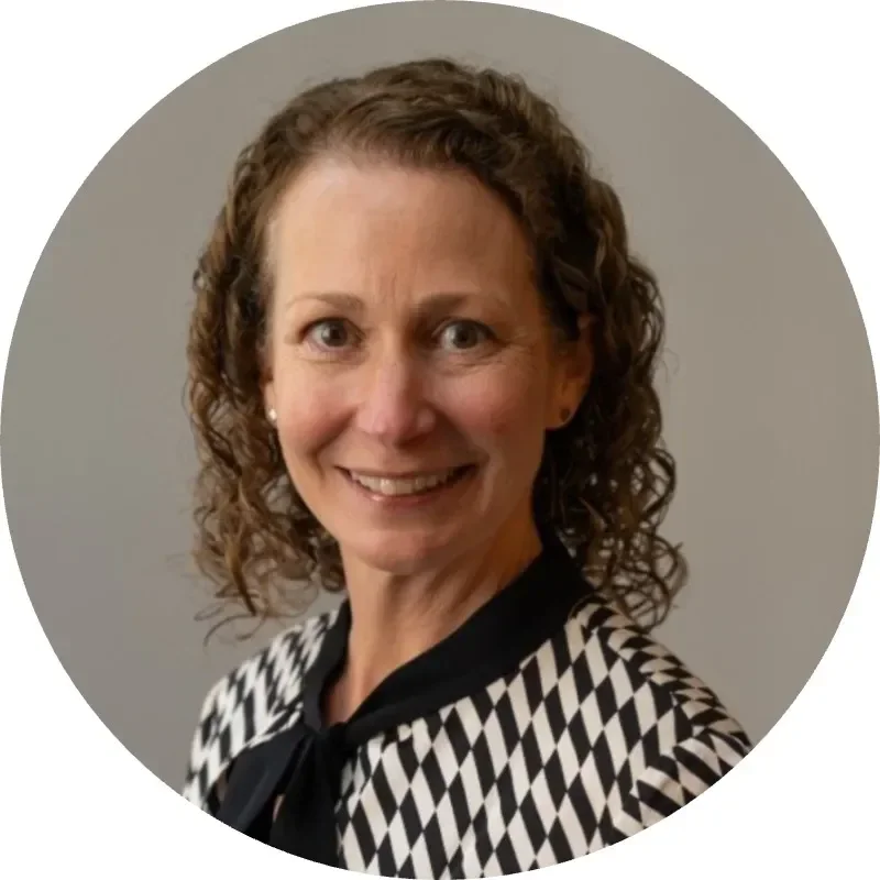 A woman with curly hair smiles, wearing a black-and-white patterned blouse.