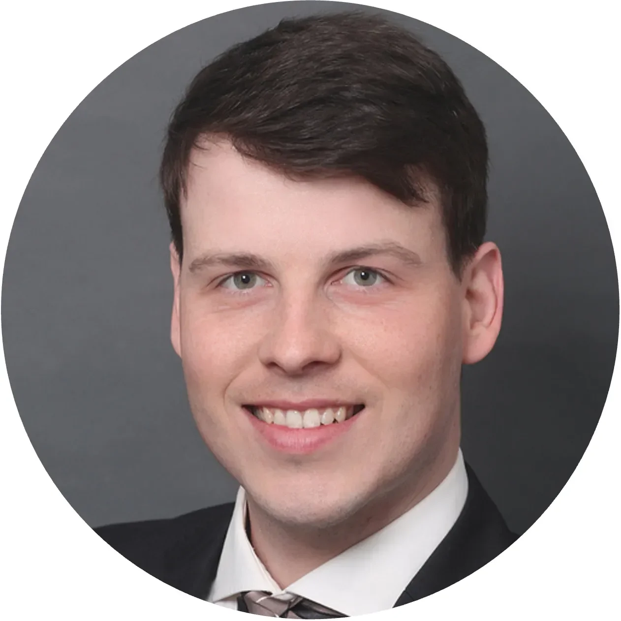 A young man with dark hair and a suit smiles warmly against a dark background.