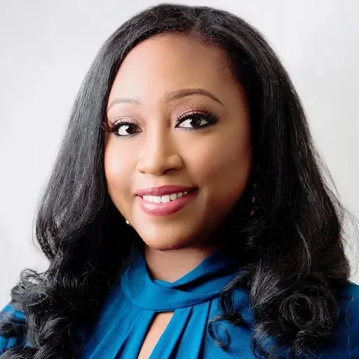 Smiling woman with long, wavy hair wearing a blue blouse, against a light background.