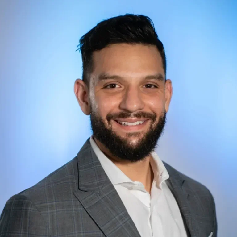 Smiling man with a beard, wearing a blazer, against a blue background.