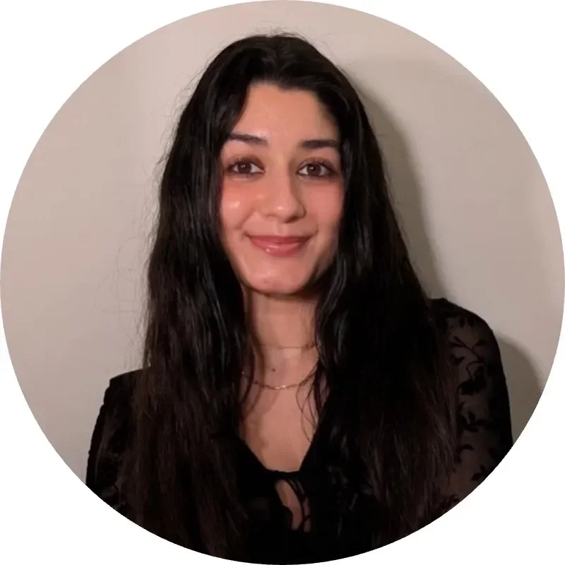 Young woman with long, black hair, smiling softly, wearing a black top against a light background.
