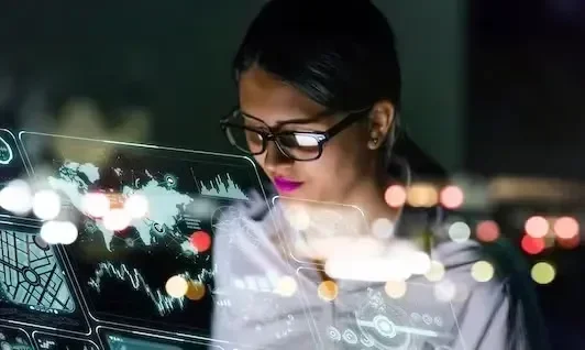 A woman in glasses looks at data visuals with city lights blurred in the background.