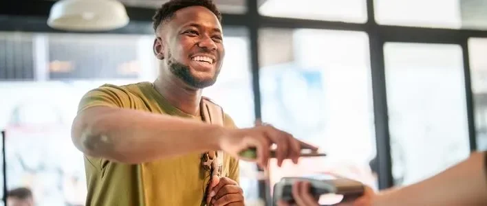 Smiling man in a green shirt making a payment at a cafe counter.