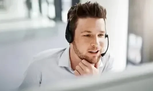 A man with a headset smiles while looking at a computer screen.