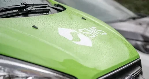 Close-up of a green vehicle hood with a white SMS logo, wet from rain.