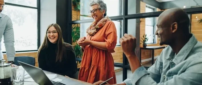 Group of people in a bright office, engaged in a joyful conversation and collaboration.