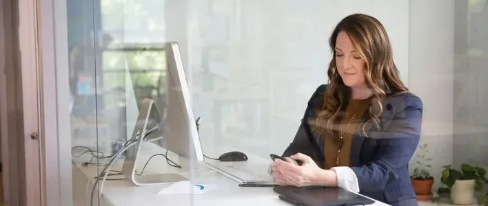 A woman with long brown hair sits at a desk, holding a pen and looking thoughtfully at her notes.