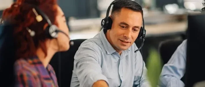Two call center employees engaged in conversation, both wearing headsets.