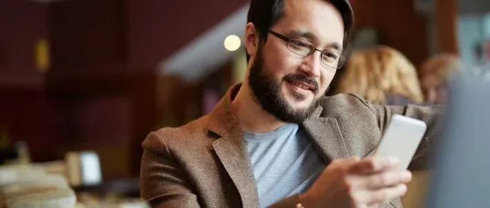Man smiling while using a smartphone in a cozy café setting.