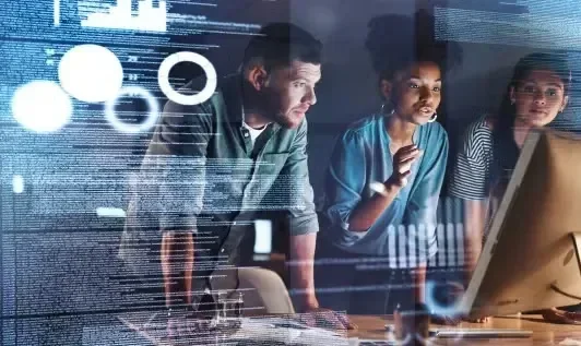 Three individuals analyze data on a computer screen, surrounded by digital graphics and charts.