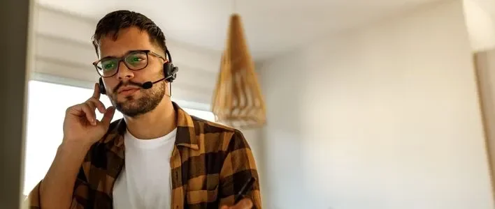 Man with glasses in a plaid shirt wearing a headset on a phone call.