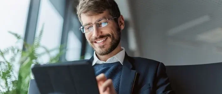 Man with brown hair and glasses smiling while looking at a tablet.