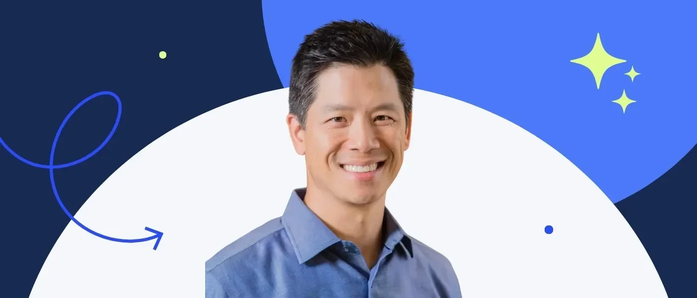 Smiling man with short black hair, wearing a blue shirt, against a colorful background.