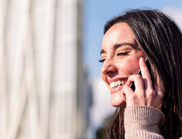 Smiling young woman talking on her phone, with modern buildings in the background.