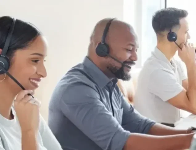 Three customer service representatives wearing headsets, smiling and working at desks.