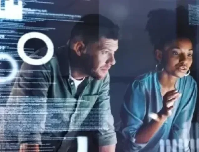 Three diverse individuals collaborate at a computer, analyzing data on the screen.