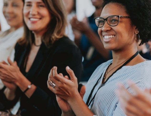 A diverse group of people clapping and smiling at an event.
