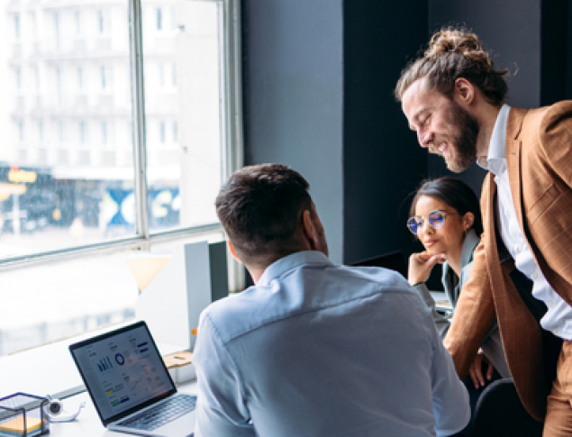 Three professionals collaborate in a bright office, with a laptop and city view.