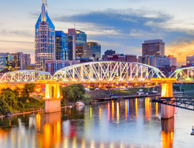 Nashville skyline at sunset, with illuminated buildings and a bridge over the river.