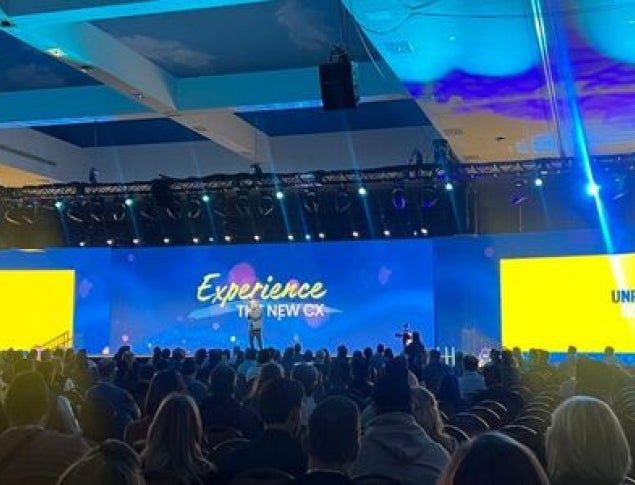 Conference setting with a large audience and colorful stage backdrop.
