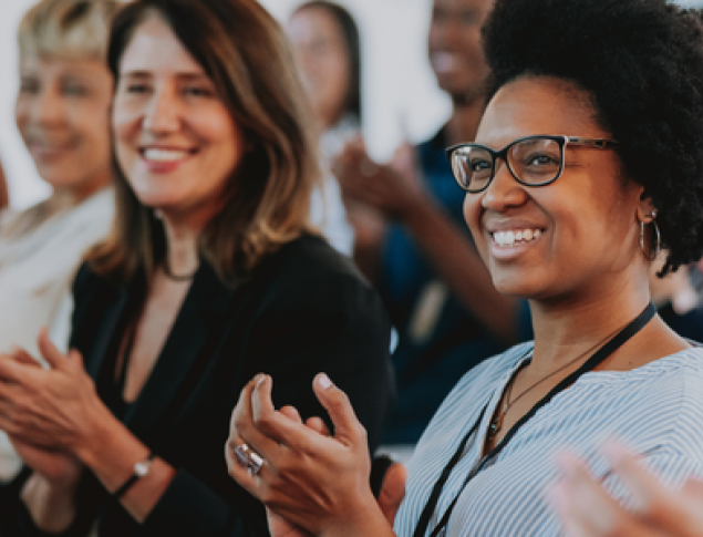 A diverse group of people smiling and clapping, showing enthusiasm and support.