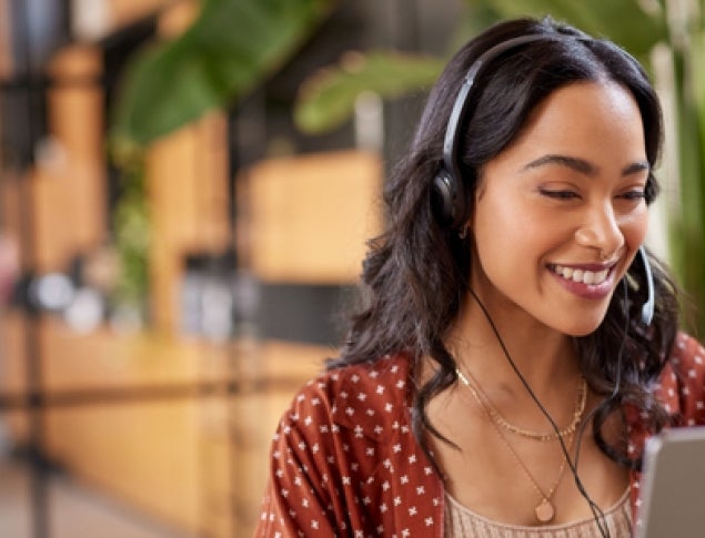 Smiling woman with headphones working on a laptop in a bright, modern office.