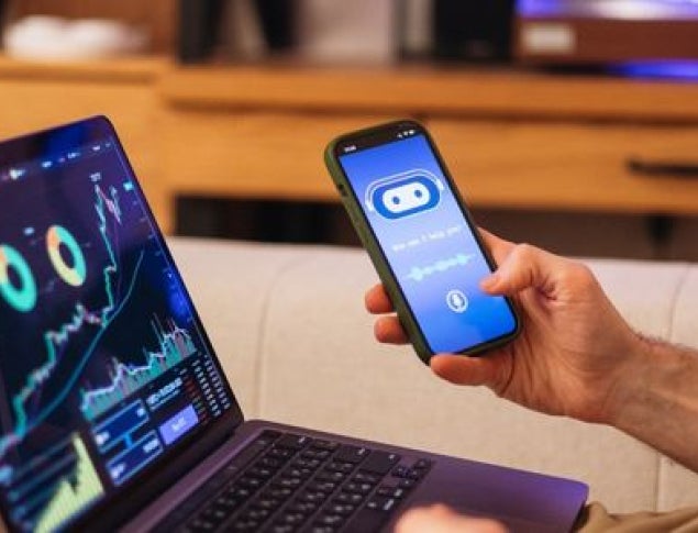 A person using a smartphone while viewing data on a laptop screen at home.