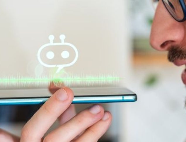 A man speaks into a smartphone with a holographic robot icon projected above it.
