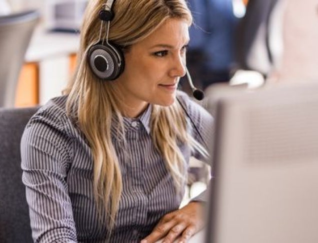 Woman wearing headphones focused on her computer in a busy office setting.