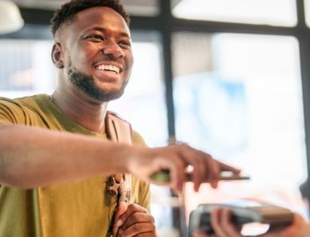 Smiling man in a green shirt making a payment at a cafe counter.