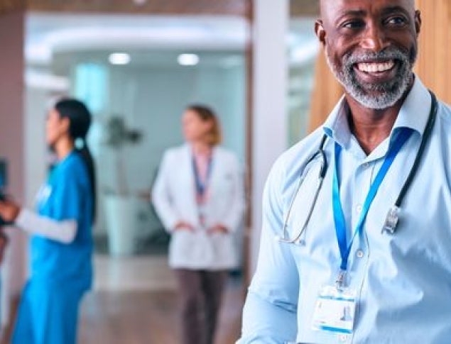 Smiling Black male doctor with a stethoscope in a modern healthcare setting.