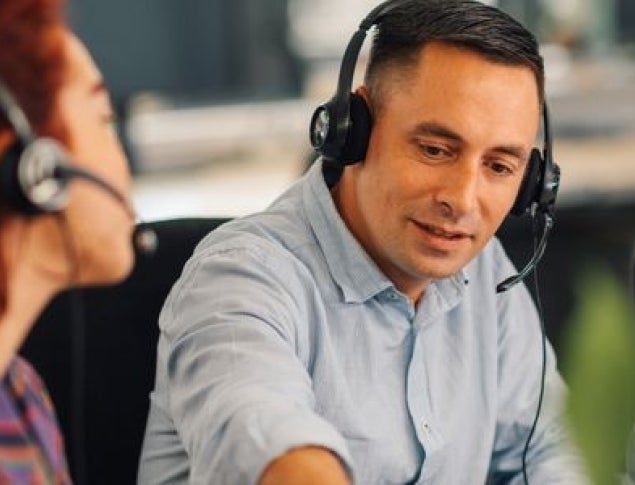Two call center employees engaged in conversation, both wearing headsets.