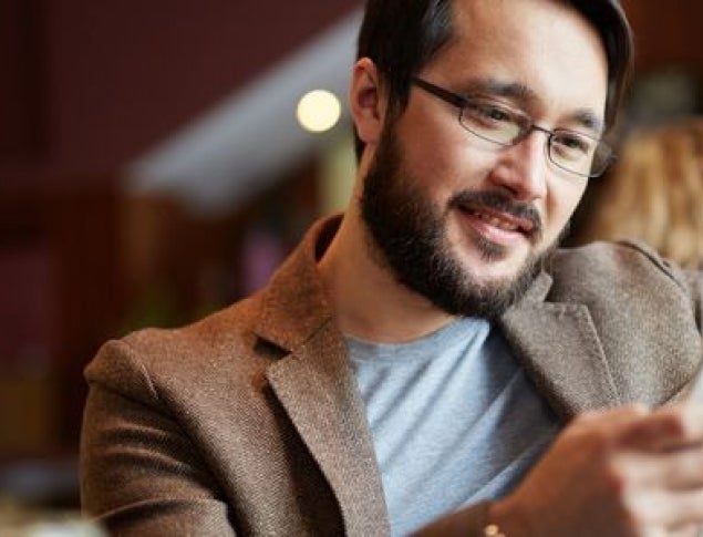 Man smiling while using a smartphone in a cozy café setting.
