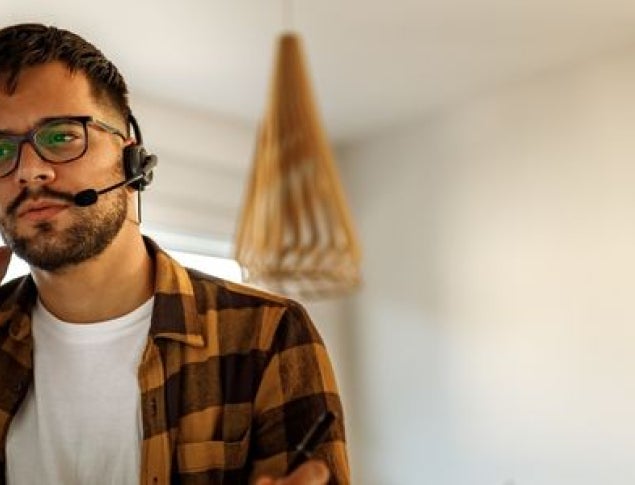 Man with glasses in a plaid shirt wearing a headset on a phone call.