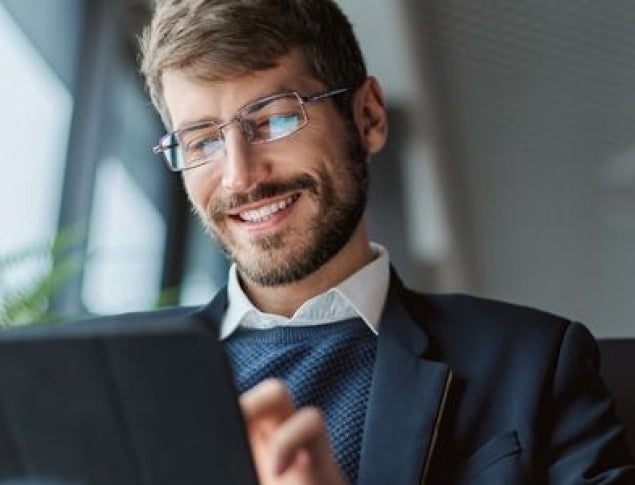 Man with brown hair and glasses smiling while looking at a tablet.