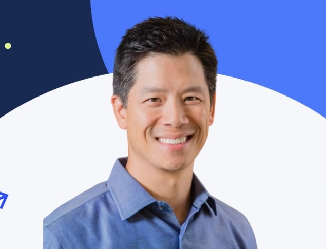 Smiling man with short black hair, wearing a blue shirt, against a colorful background.